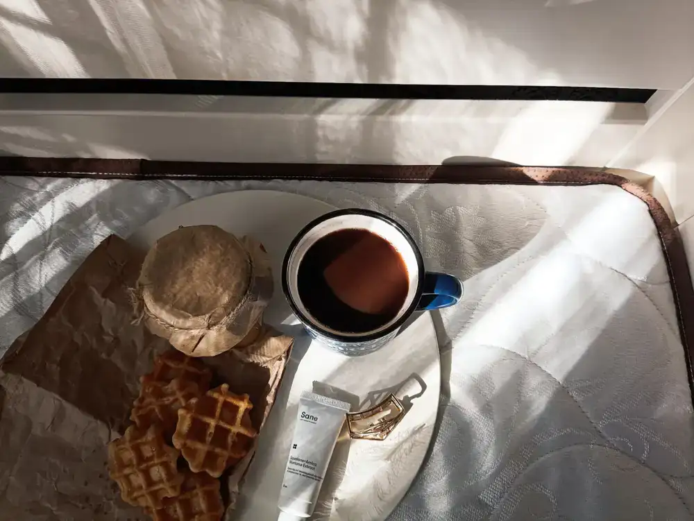 A steaming mug of coffee next to a wooden tray of neat, bite-sized pastries on a wooden table